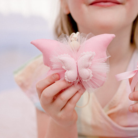 A child holding a pink butterfly-shaped Tooth Fairy pouch with a pouch for the tooth and coin at the back.